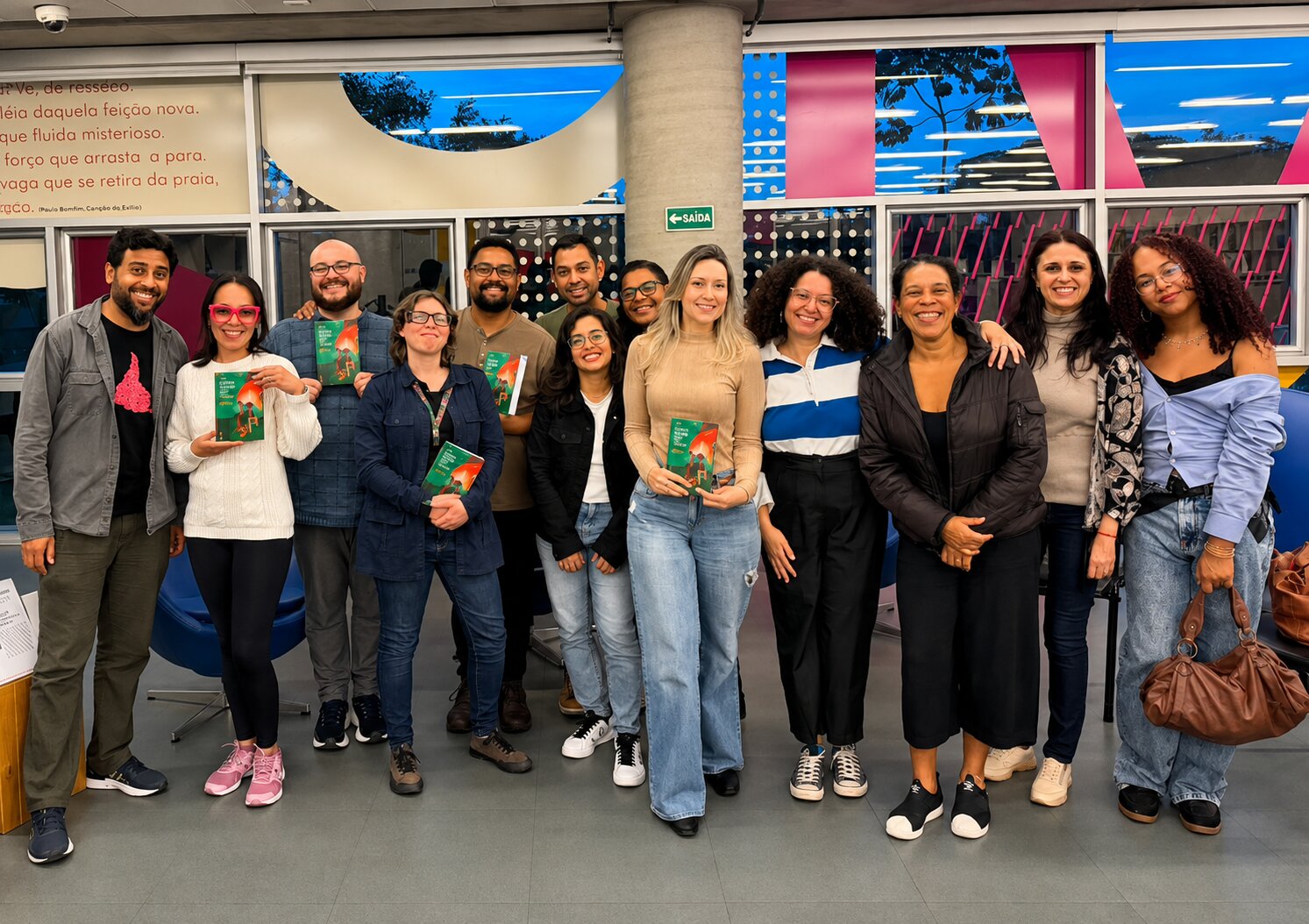 Grupo do clube de leitura reunido, cada pessoa segurando um exemplar do livro do ciclo